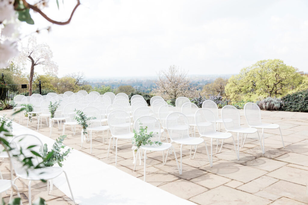 Rows of white chairs and a long white carpet on a patio.