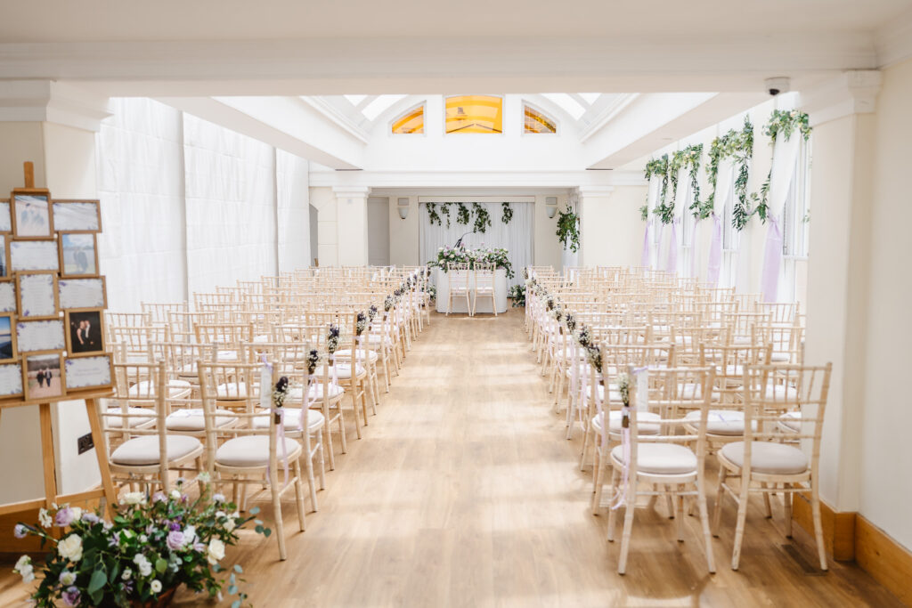 A large room with an easel, flower arrangements and rows of chairs.