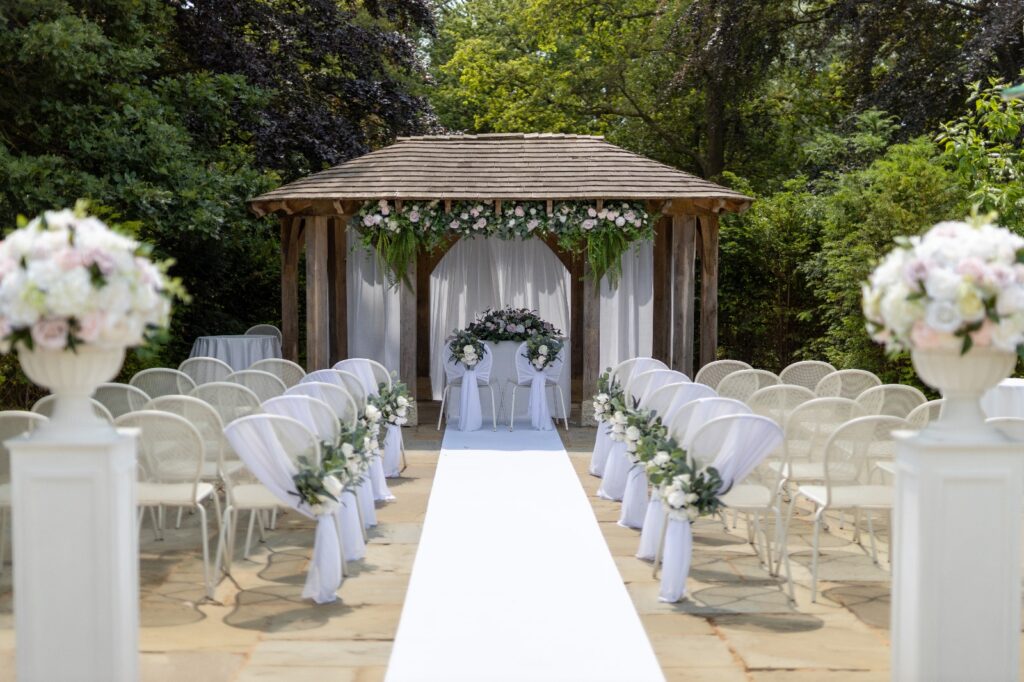 A large wooden wedding arch with rows of white chairs and a long white carpet.