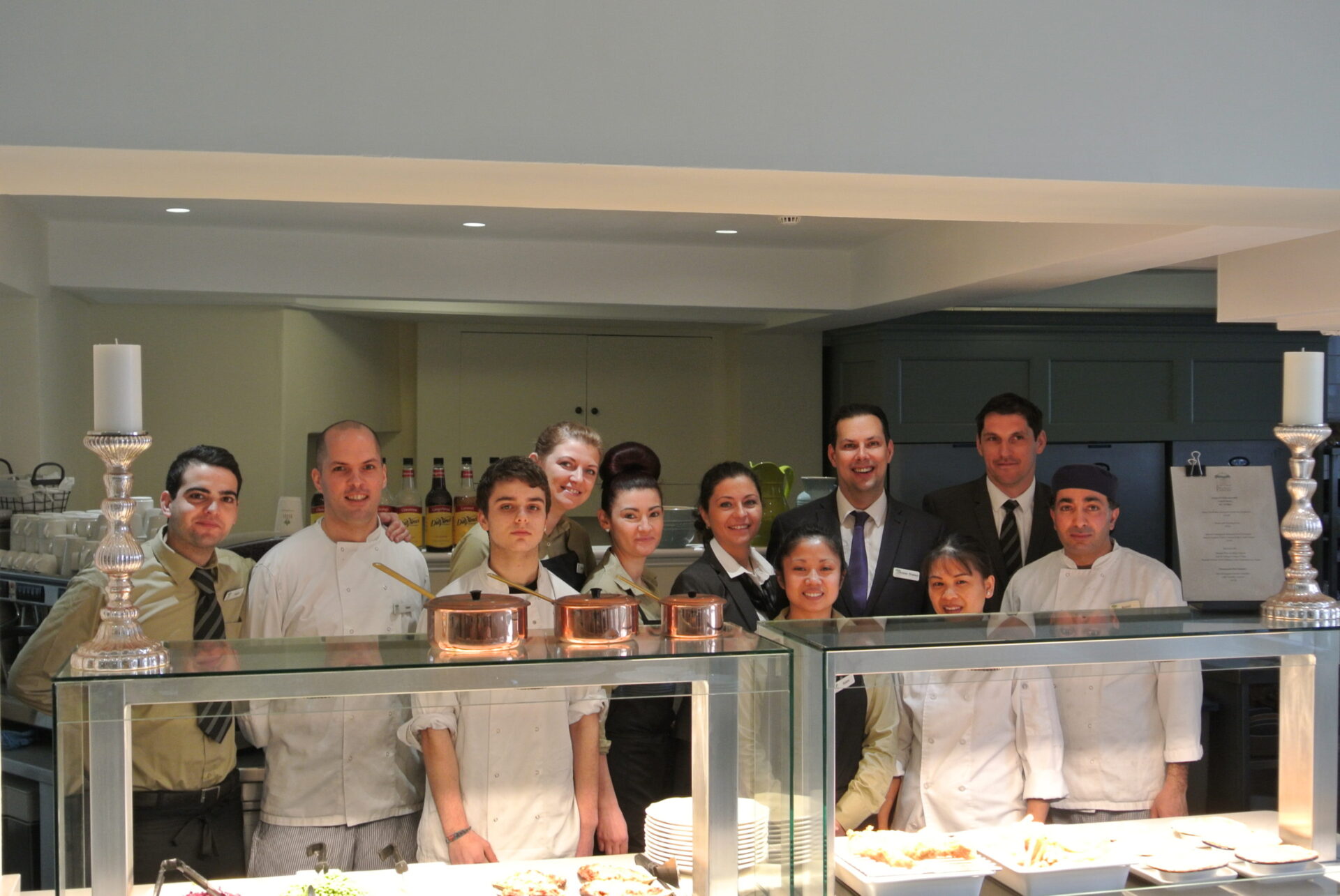 A group of kitchen staff smiling behind food serving stations.