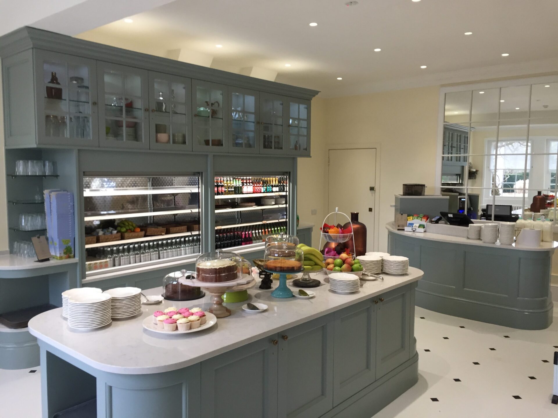 A modern kitchen area with grey units and cakes under glass covers.