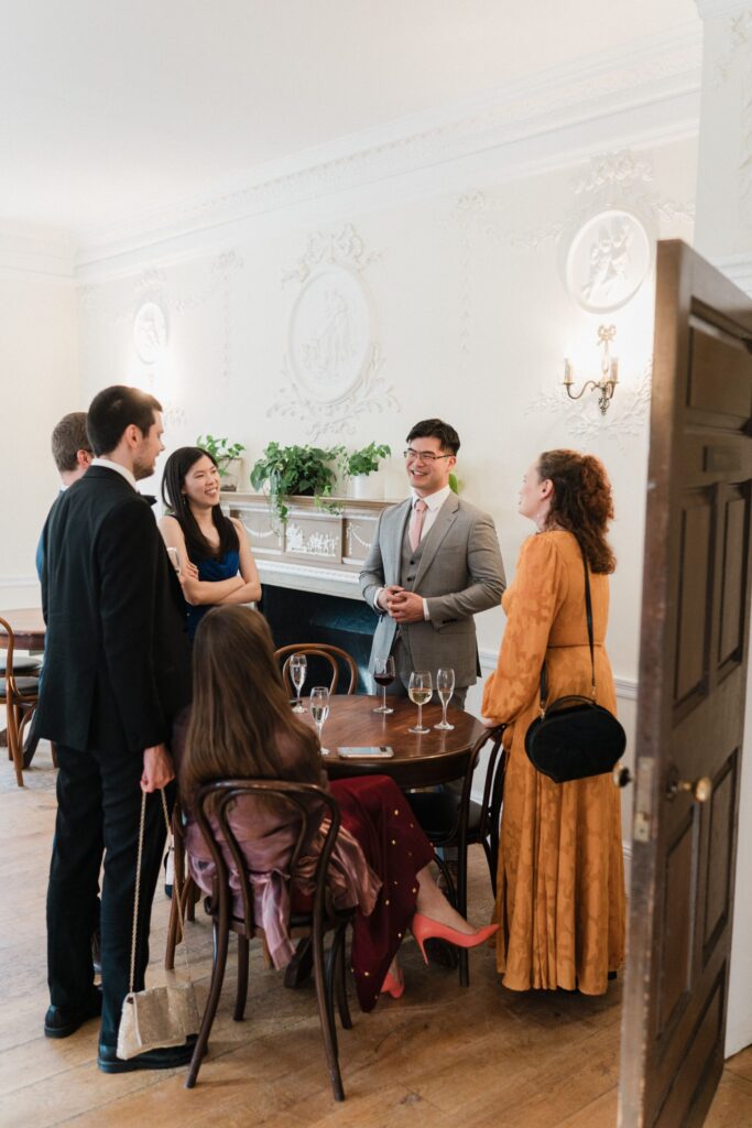 A group of people stood around a wooden table talking.