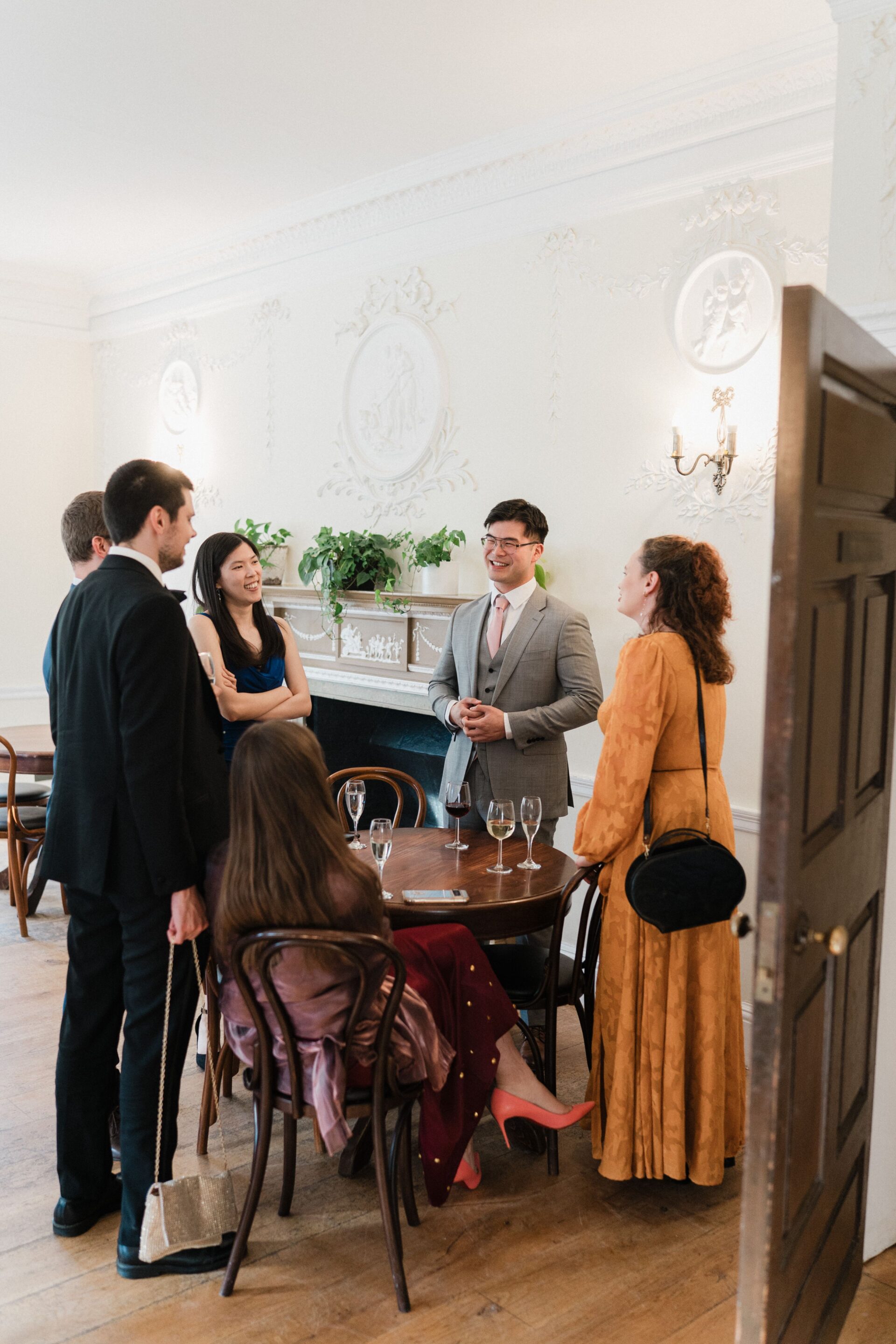 A group of people stood around a wooden table talking.