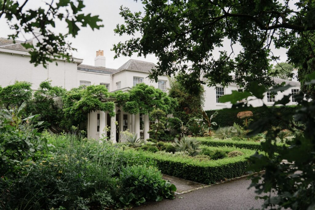 A lush green garden with a white Georgian building.