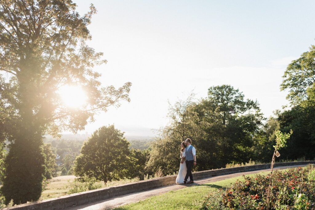 A bride and groom embracing in parkland.