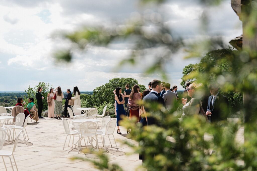 A large patio with tables and chairs and wedding guests talking.