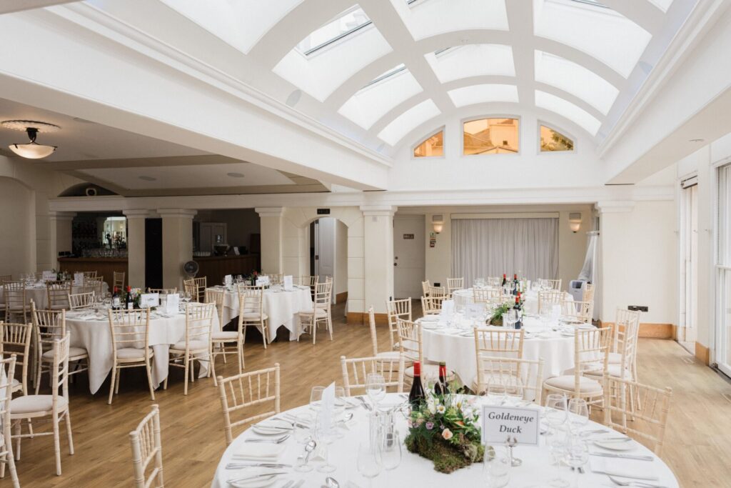 A bright large venue room with white round tables.
