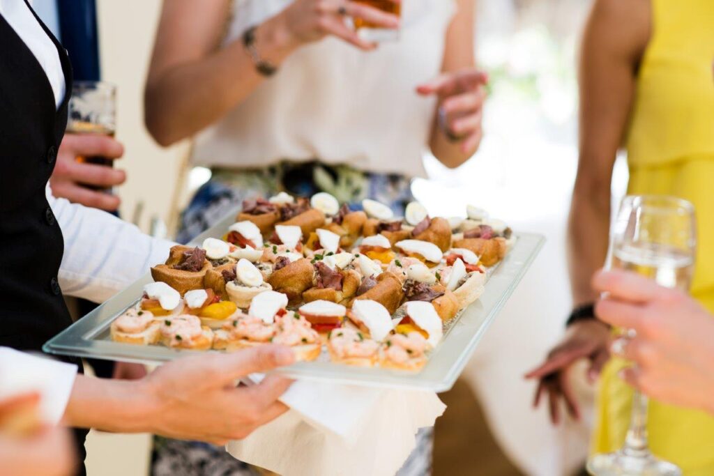 A waiter serves an elegant tray of assorted canapés to formally dressed guests at a gathering.